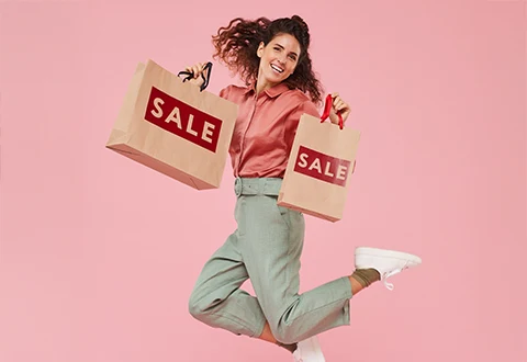 Imagem de mulher sorridente a saltar de alegria com sacos de compras “SALE” num fundo rosa. Representa o entusiasmo e aumento de vendas durante o Prime Day da Amazon.